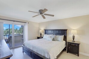 A bedroom with a bed, two bedside tables with lamps, a ceiling fan, and a sliding glass door leading to a balcony.