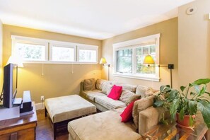 A living room with a sofa, ottoman, TV, and lamps.