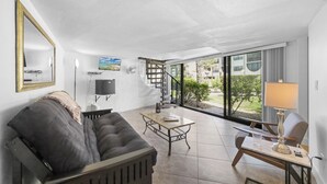 Una sala de estar moderna con un sofá, una mesa de centro y una lámpara. Se ve una ventana grande con vistas a zonas verdes y edificios.