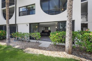 A modern building with a circular window, a patio area with a table and chairs, and a well-maintained garden with trees and shrubs.
