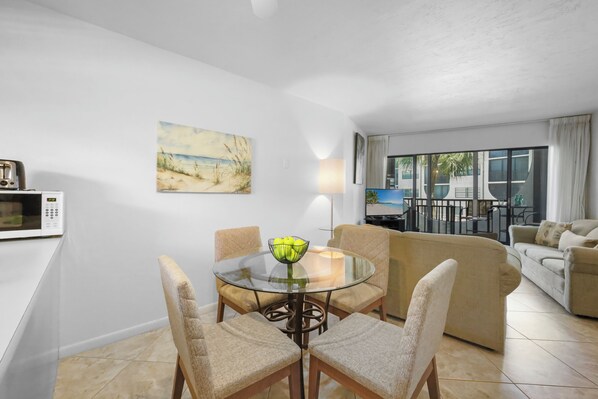 A living room with a glass table, beige chairs, a sofa, and a painting on the wall.
