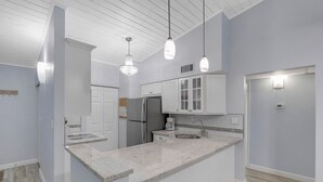 A modern kitchen with white cabinetry, a marble countertop, and pendant lighting. - Charming Condo | Two Pools and Steps to Beach (Marco Island)