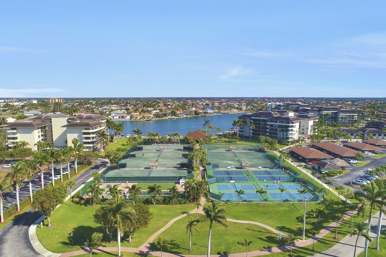 A resort with multiple tennis courts, a body of water, and surrounding buildings.