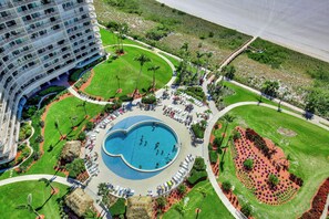A hotel with a large pool surrounded by a landscaped garden, a beach, and a parking area.