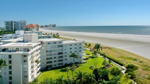 A beachfront hotel with multiple floors, a well-maintained lawn, and a view of the ocean. - Magical Beachfront Condo | Pool & Ocean Views (Marco Island)
