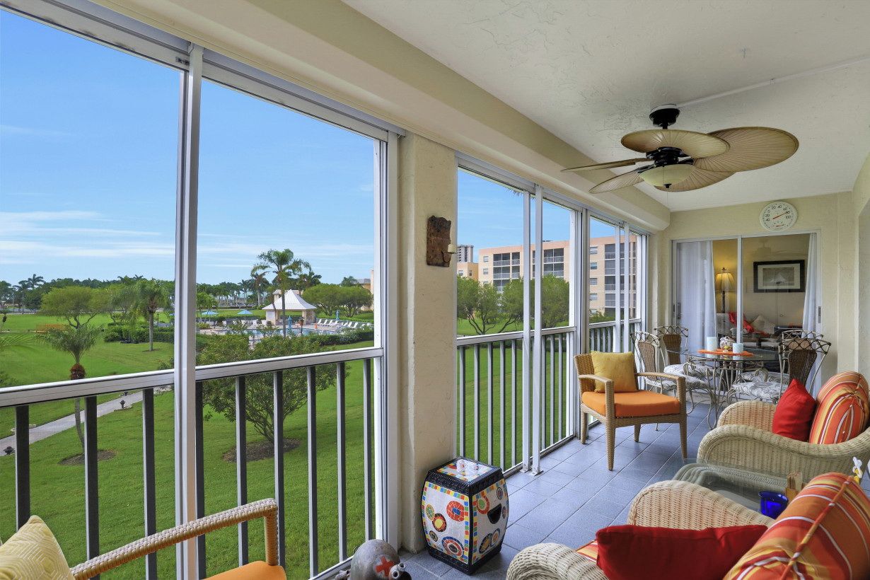 A spacious balcony with large windows, wicker furniture, and a ceiling fan.