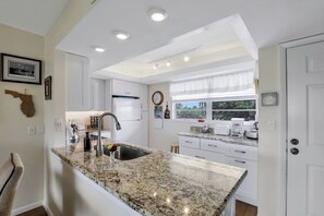 A modern kitchen with granite countertops, white cabinetry, and a built-in oven. - Island-Style Condo | Pool, Spa & Steps to Beach (Marco Island)