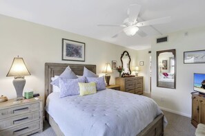 A bedroom with a bed, nightstands, a ceiling fan, a TV, and a mirror. - Island-Style Condo | Pool, Spa & Steps to Beach (Marco Island)