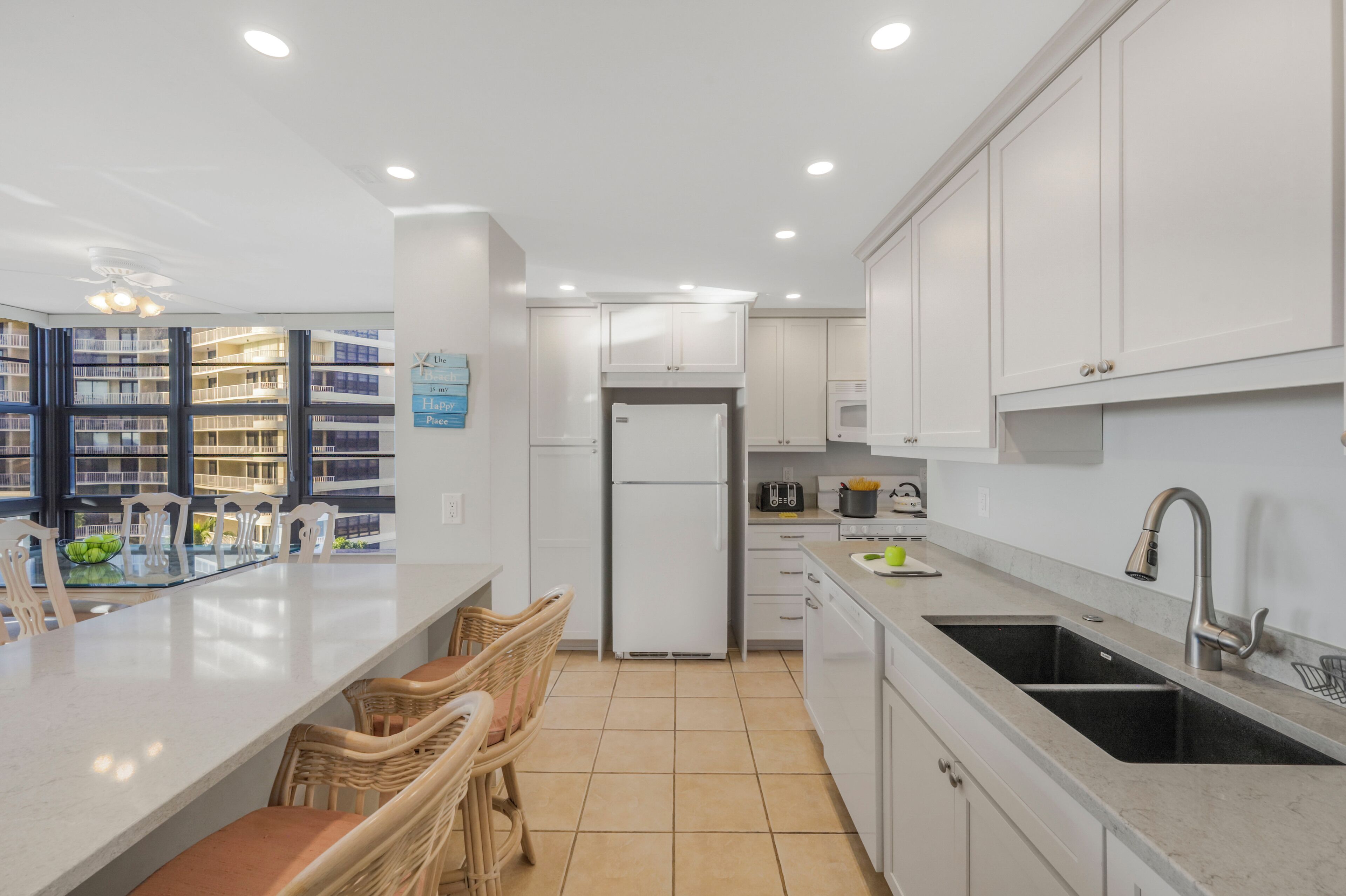 Cozinha moderna com armários brancos, ilha central com assentos, geladeira e micro-ondas.