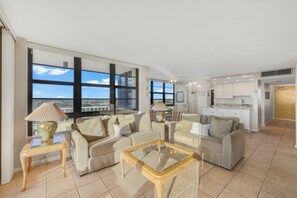 A spacious living area with large windows, a kitchen, and a dining area. - Beachfront Condo | Pool/Views from Two Balconies (Marco Island)