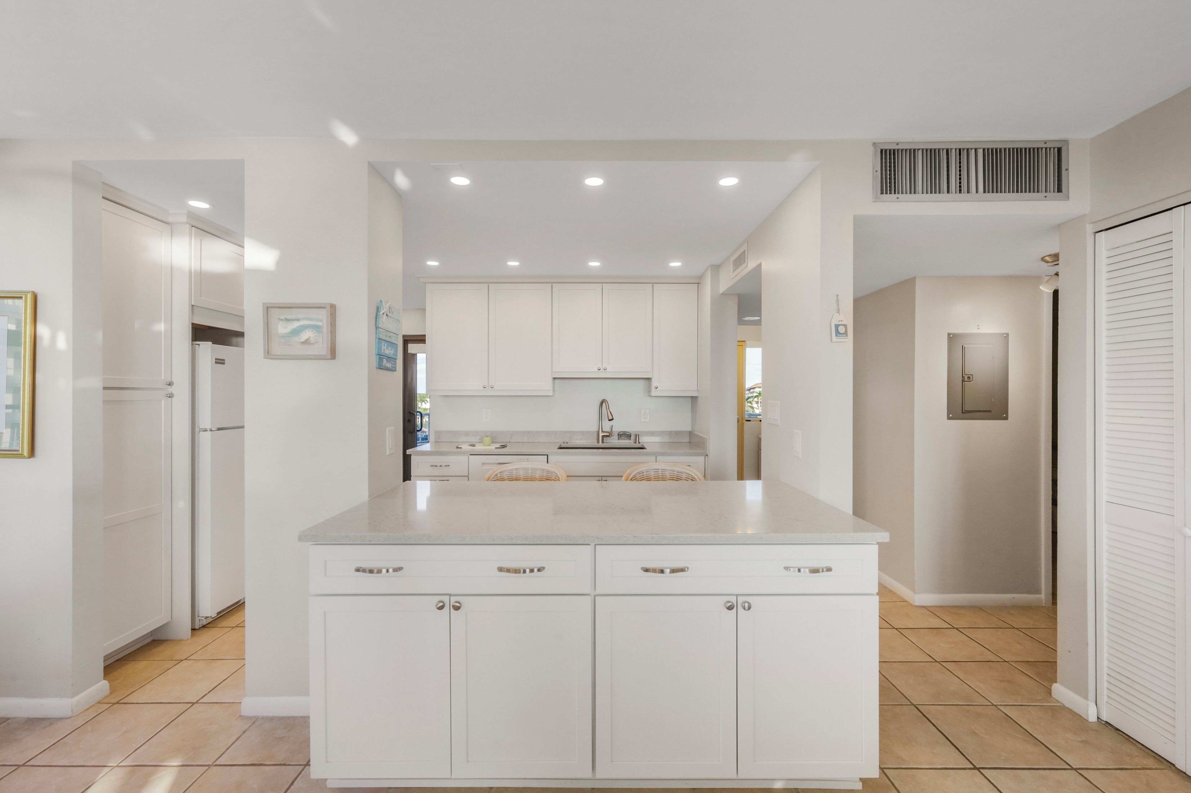 Una cocina moderna con armarios blancos, una isla central y luces empotradas en el techo.