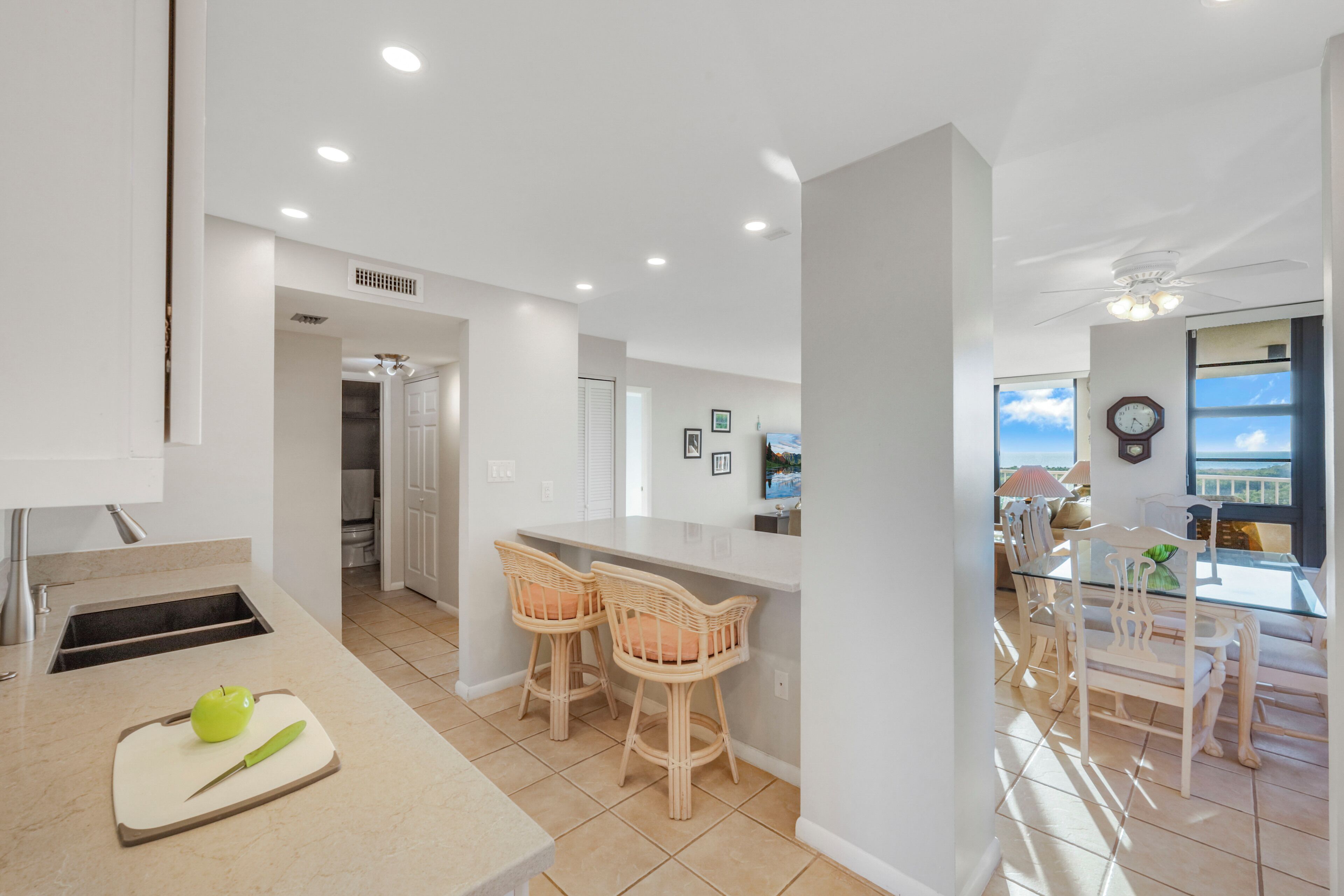 A modern kitchen with a bar area, two wicker chairs, and a dining table with chairs.
