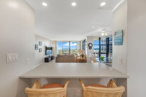 A modern kitchen with a central island, wicker chairs, and a view of the ocean. - Beachfront Condo | Pool/Views from Two Balconies (Marco Island)