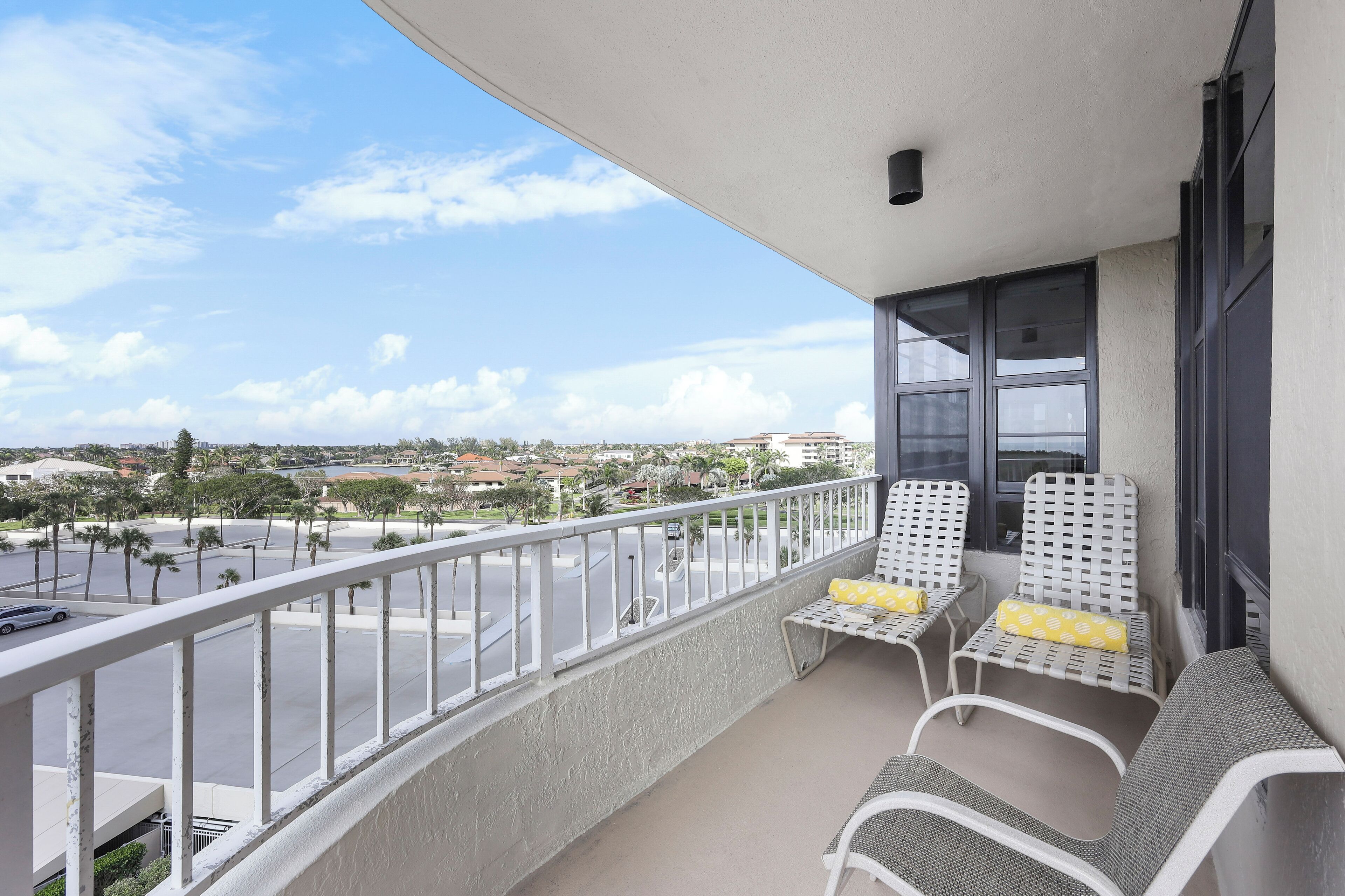 Un balcon avec des chaises blanches et une table, donnant sur une rue et des immeubles.