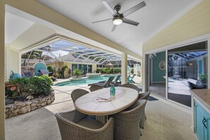 Un patio techado con piscina, mobiliario exterior y ventilador de techo.