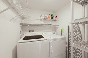 A laundry area with a washer and dryer, shelves with cleaning supplies, and a patterned shelf unit.