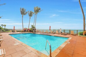 A rectangular pool with a metal ladder, surrounded by lounge chairs and palm trees, with a view of the ocean.