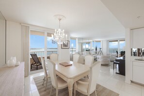 A spacious living area with a dining table, chairs, a chandelier, and a balcony with a view.