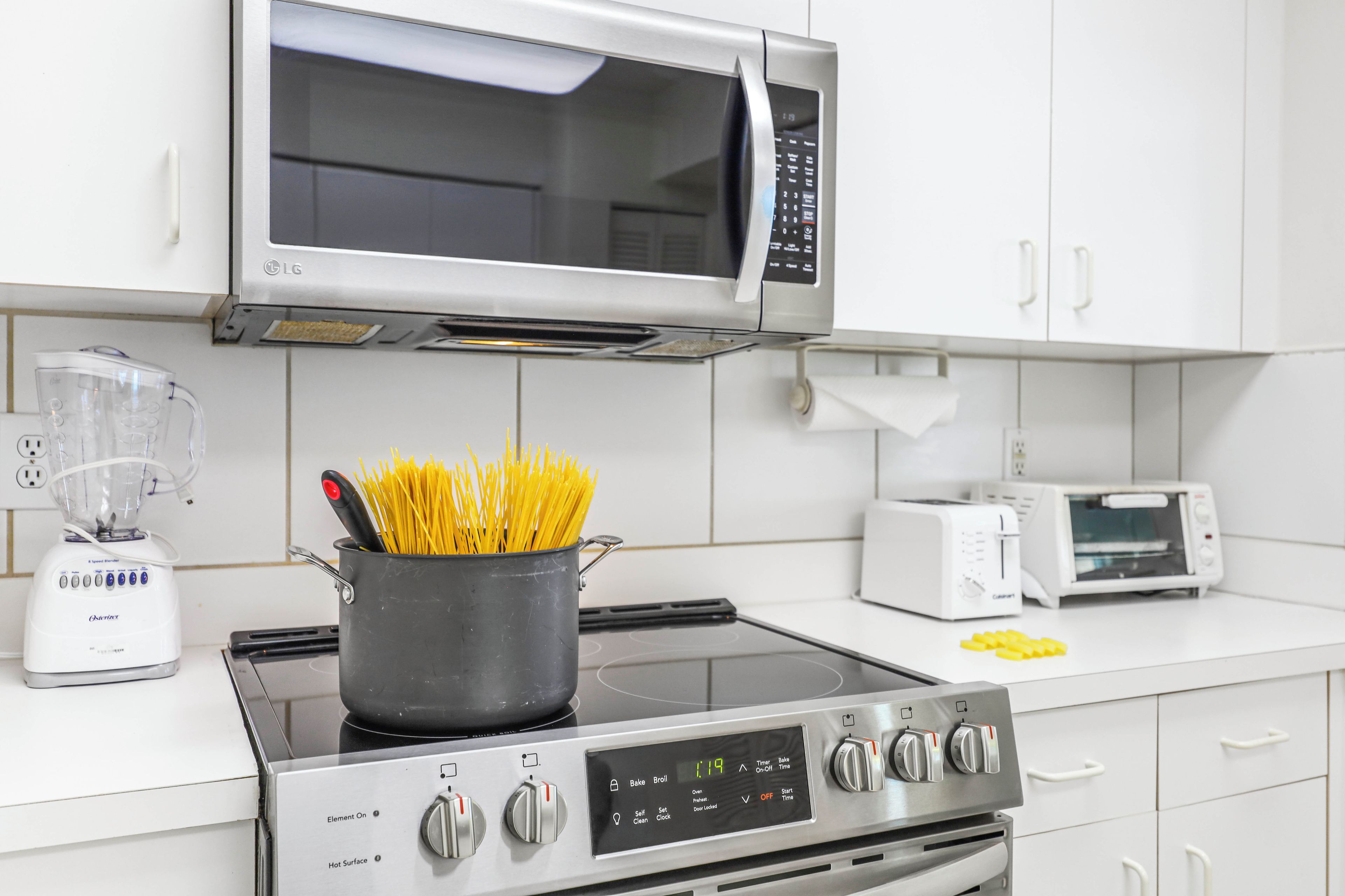 Une cuisine équipée d’une cuisinière, d’un four à micro-ondes, d’un grille-pain et d’une casserole de spaghettis.