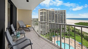 Ein Balkon mit Blick auf einen Pool, Liegestühle und ein Hochhaus im Hintergrund.