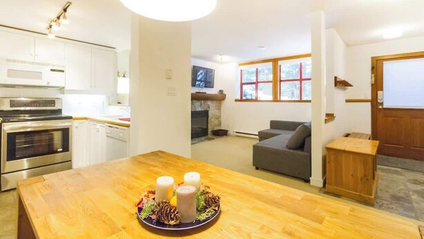 A modern kitchen with built-in appliances, a dining area with a wooden table, and a cozy living space with a fireplace. - Cozy Retreat in The Woods, Hot Tub & Free Parking (Whistler)