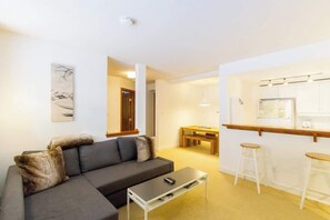 Una sala de estar moderna con un sofá gris, una mesita de centro y una zona de comedor con una mesa de madera y taburetes de bar.