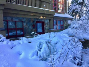 Un edificio de fachada de piedra, ventanas con marcos rojos y un paisaje cubierto de nieve.