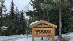 A wooden sign with the text 'The WOODS 4652 BLACKCOMB WAY' in a snowy environment. - Cozy Retreat in The Woods, Hot Tub & Free Parking (Whistler)