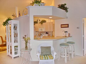 A compact kitchen with a white island, bar stools, and a wicker chair. - Quiet, Gated Community | Pool and Tennis Courts (Marco Island)
