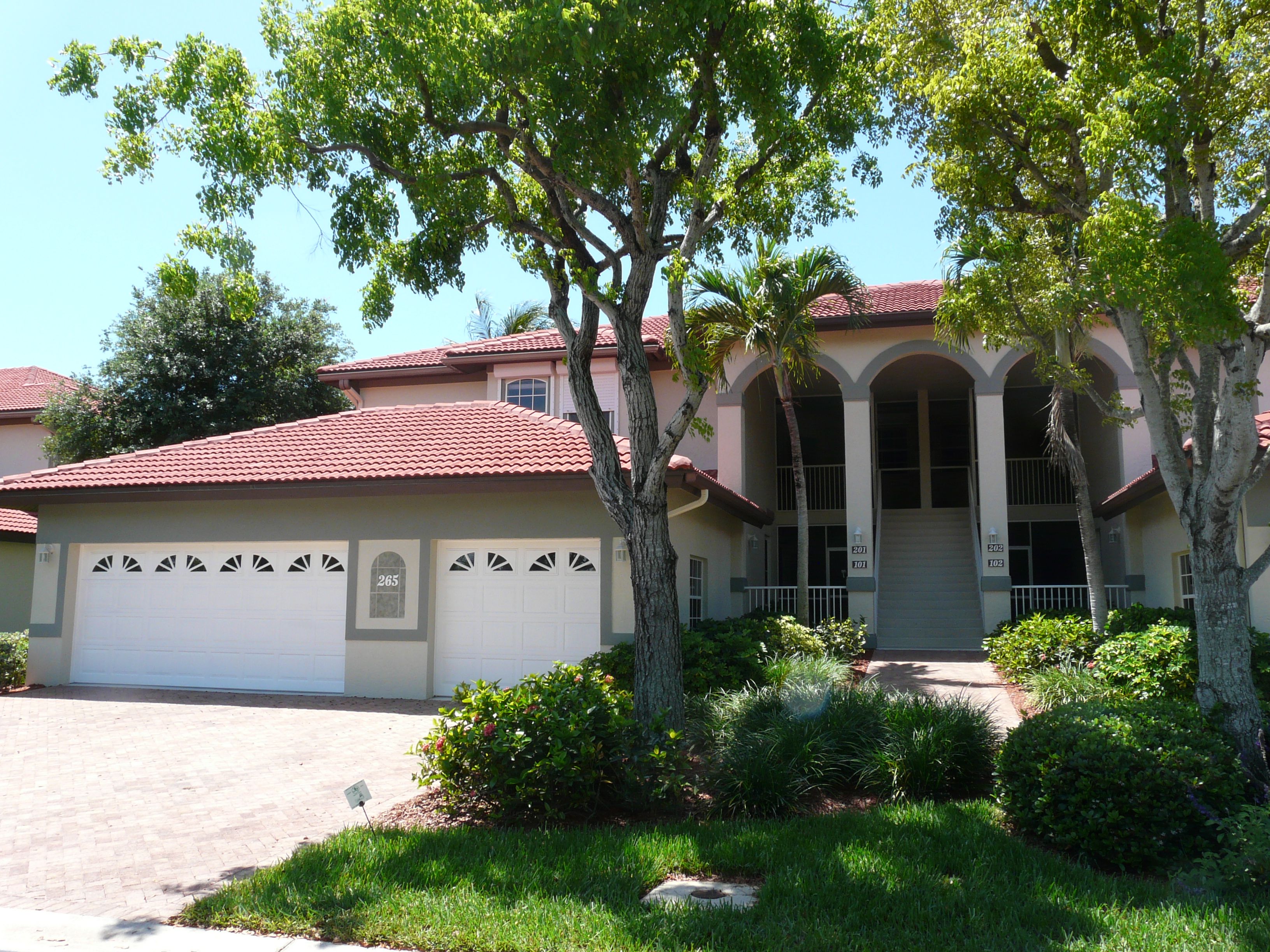 A two-story house with a red-tiled roof, a garage, and a well-maintained front yard with trees and shrubs.