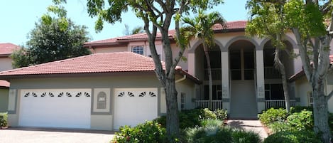 A two-story house with a red-tiled roof, a garage, and a well-maintained front yard with trees and shrubs.
