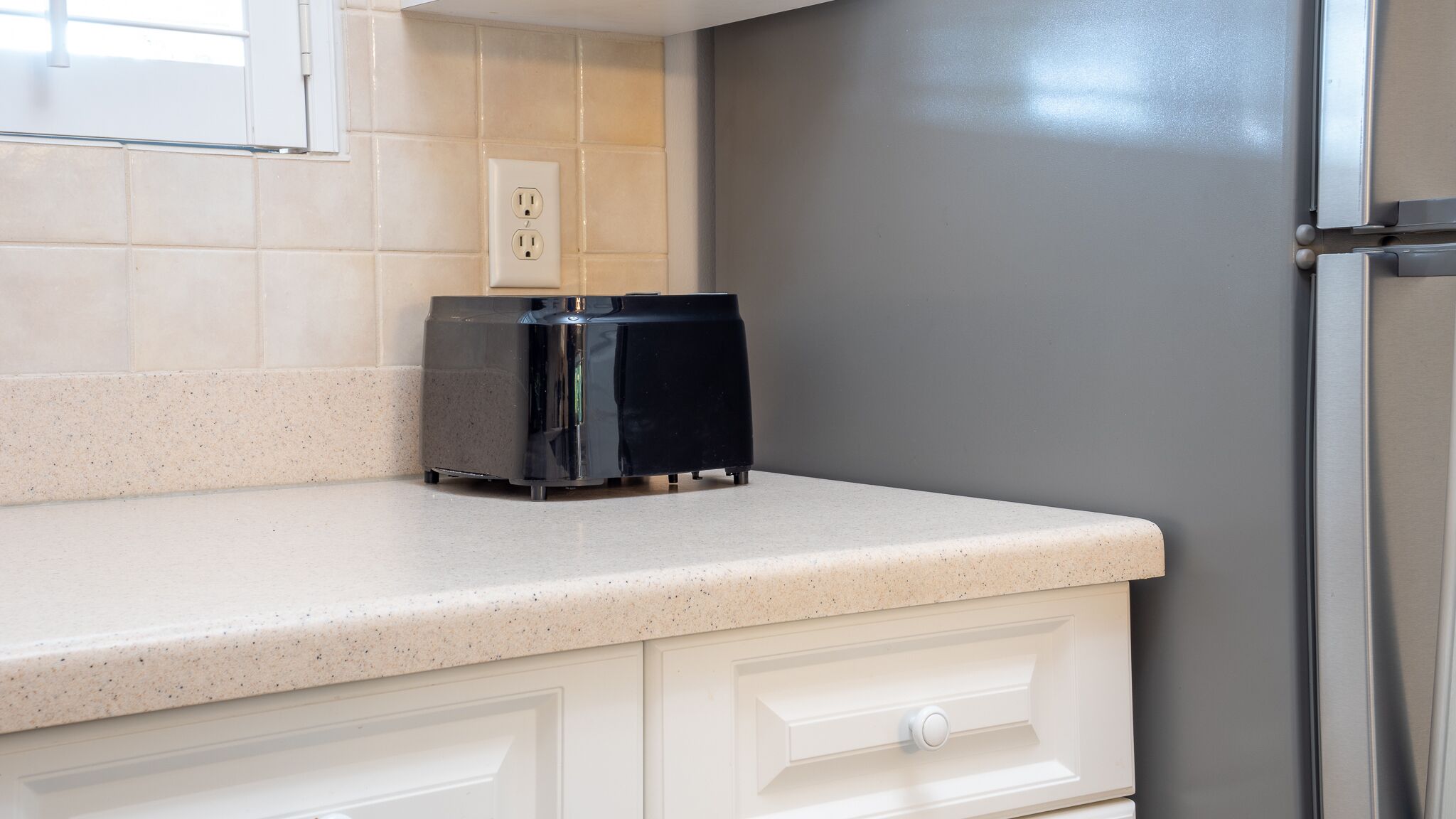 Una cocina con encimera, cafetera, armario blanco y pared gris.
