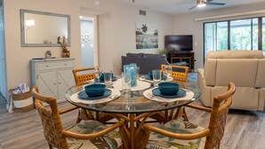 Een eethoek met een ronde glazen tafel, blauw servies en rieten stoelen.