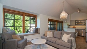 Una sala de estar moderna con un sofá gris, una mesa de centro redonda y ventanas amplias con vistas a zonas verdes.