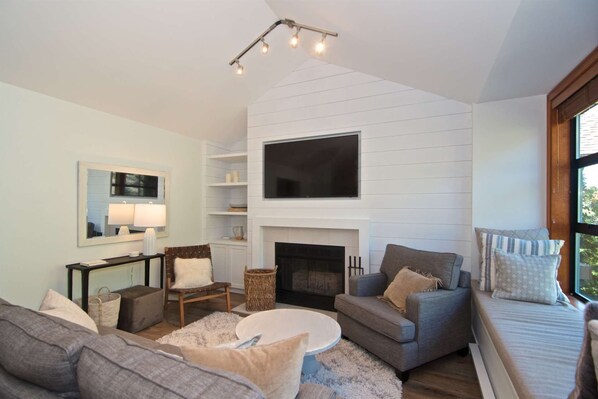 A living room with a fireplace, sofas, a coffee table, and a TV mounted on the wall.