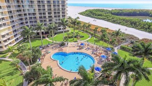 Um hotel com uma piscina grande, palmeiras e vista para a praia.