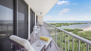 Varanda com vista para uma praia e água, um banco com um livro e duas cadeiras.