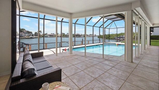 A spacious indoor area with a large glass wall offering a view of a swimming pool and a body of water.