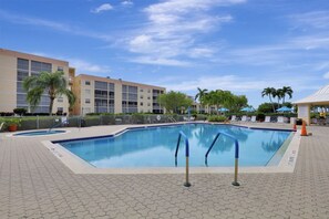 A swimming pool with a tiled deck, surrounded by palm trees and a building with multiple balconies.