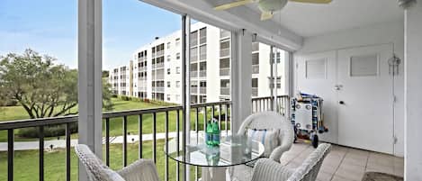 A balcony with wicker furniture, a ceiling fan, and a view of a building complex.