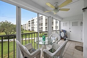 A balcony with wicker furniture, a ceiling fan, and a view of a building complex.