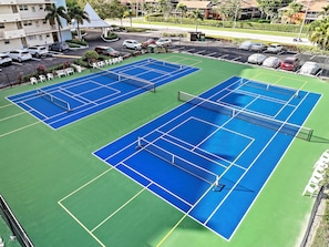 An aerial view of a tennis court complex with multiple courts, a parking area, and surrounding buildings. - Coastal Style Condo | Pool, Spa & Steps to Beach (Marco Island)