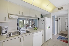 A modern kitchen with white cabinetry, a built-in dishwasher, and a refrigerator. - Coastal Style Condo | Pool, Spa & Steps to Beach (Marco Island)