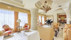 Tilava aula, jossa on suuri flyygeli, tyylikkäät nojatuolit ja koristeellinen kattokruunu.