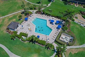 An aerial view of a swimming pool area with a rectangular pool, surrounded by lounge chairs and umbrellas, and a small building with a sloped roof. - Relaxing Condo | Pool, Bay View & Steps to Beach (Marco Island)