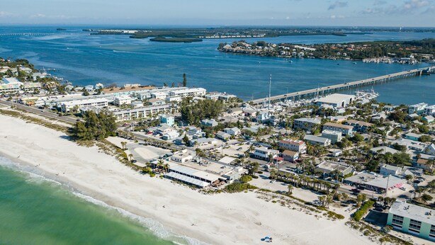 Vue aérienne d’une ville côtière avec une plage, un port de plaisance et un pont reliant la ville à une île.