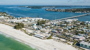 An aerial view of a coastal town with a beach, marina, and a bridge connecting to an island.