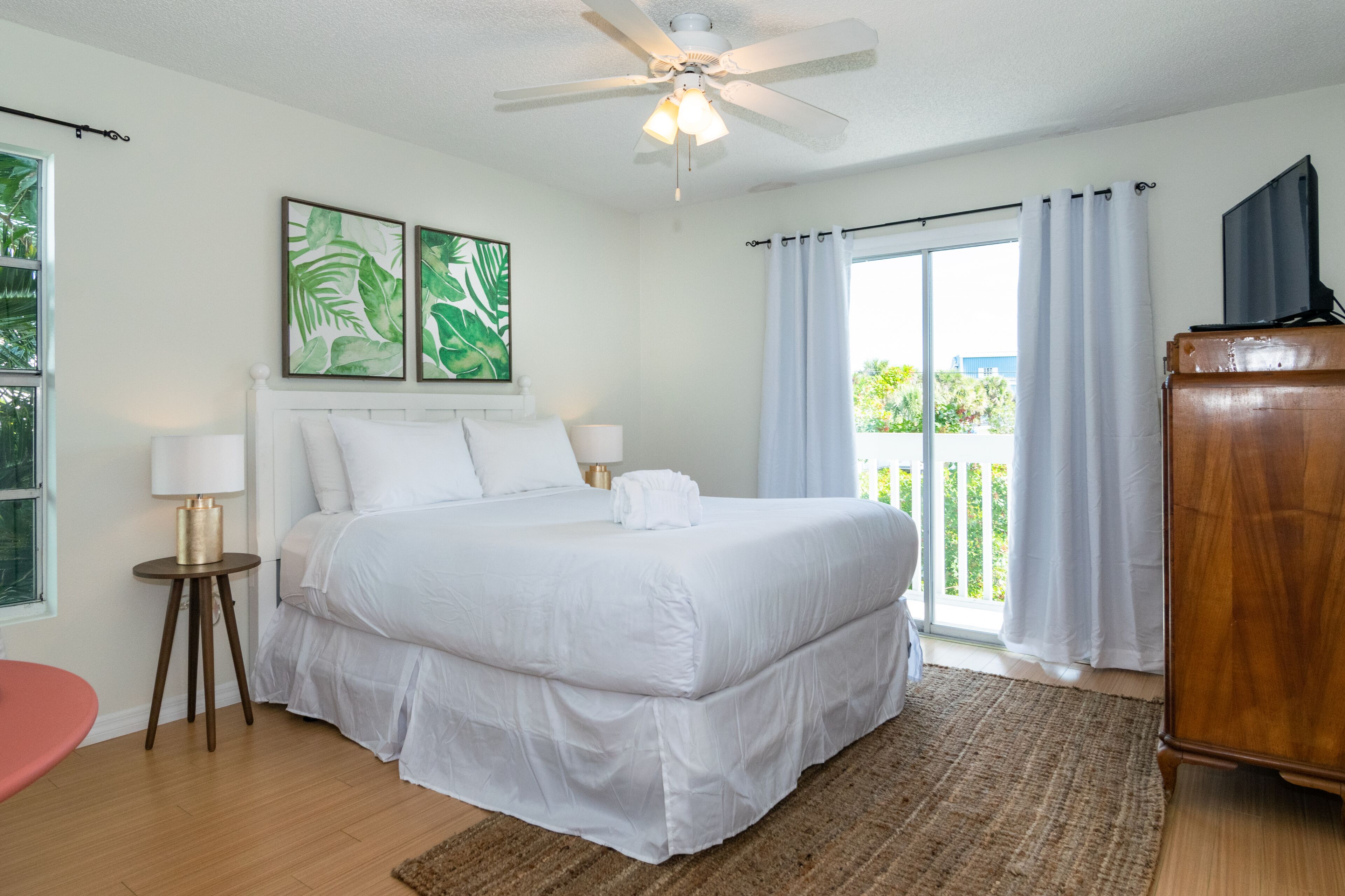 Une chambre spacieuse avec un grand lit, un ventilateur de plafond et un balcon agrémenté de rideaux.