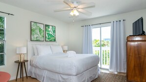 Une chambre spacieuse avec un grand lit, un ventilateur de plafond et un balcon agrémenté de rideaux.