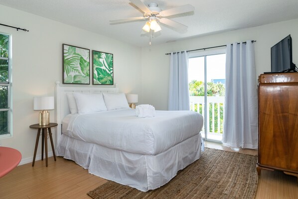 A spacious bedroom with a large bed, a ceiling fan, and a balcony with curtains.